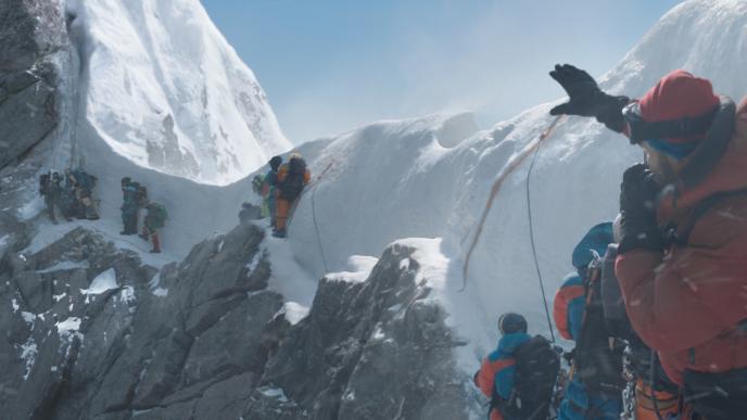 back view of people in snow suits and jackets hiking up a snowy mount everest