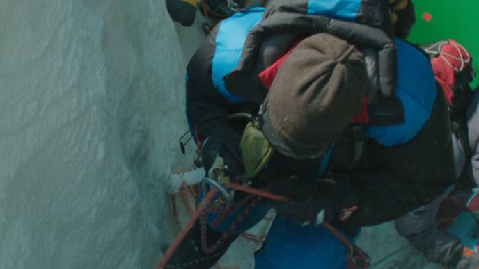 aerial shot of three actors in full hiking gear on a snowy mountain film set set in front of a green screen