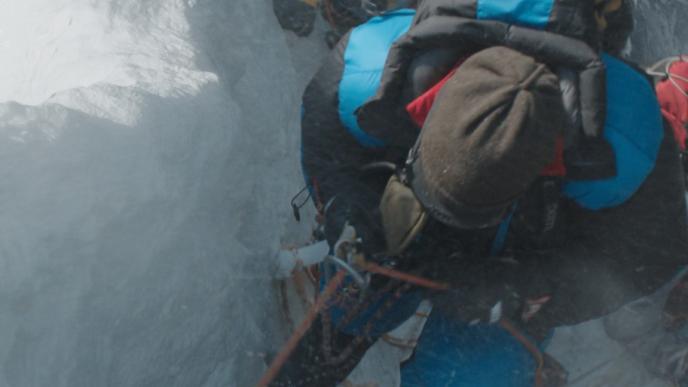 aerial view of three hikers in full hiking gear walking up a a snowy mountain