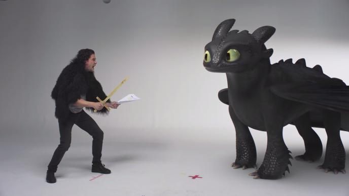 actor kit harington crouhed next to a cg animated toothless the dragon sheepishly looking at him