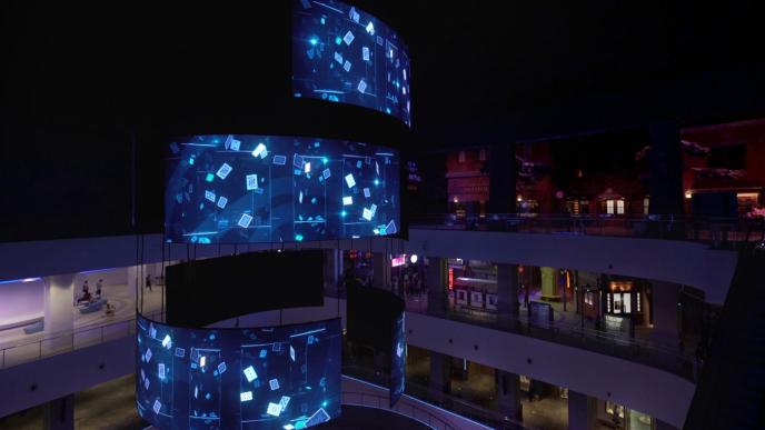 a large tower screen of play cards projected on it amongst a shopping mall