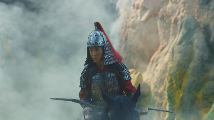 mulan actress liu yifei riding a horse in full warrior armour while holding an archery bow