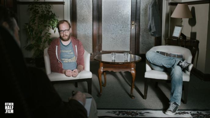 a man inside of a therapist room. him and his torso are sitting in one chair as his legs sit in the other chair next to him