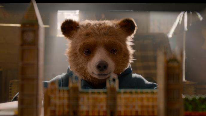 paddington bear looking at a paper mache of big ben clock tower and parliament