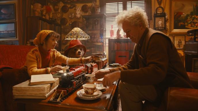 paddington bear sitting in a living room with two people