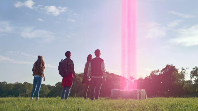 back view of teenagers standing in front of a pink portal shooting up into the sky