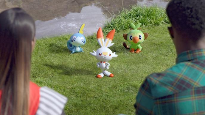 back view of teens looking at three small animated pokemon standing on the ground