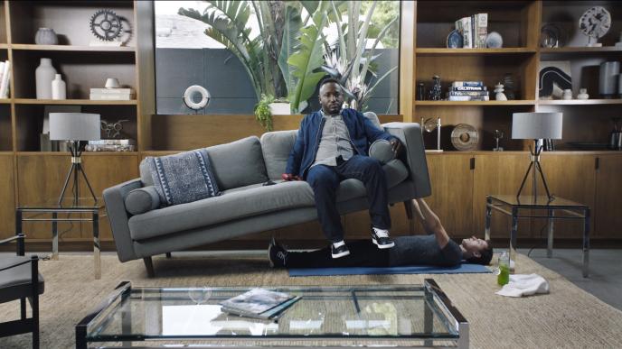 actor tom holland doing a bench press with a sofa while comedian hannibal buress is sitting