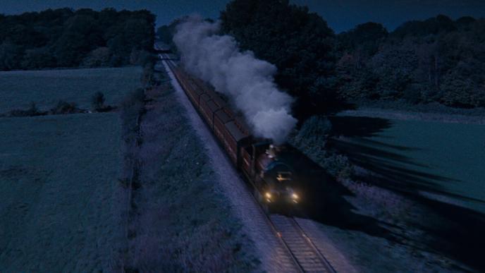 a steam locomotive dashing through train tracks set in nighttime