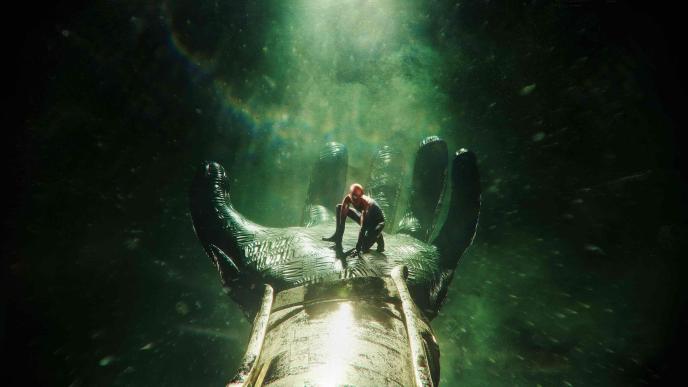 spider man crouched inside the palm of a giant hand that is wearing a leather textured glove. there is a green misty light