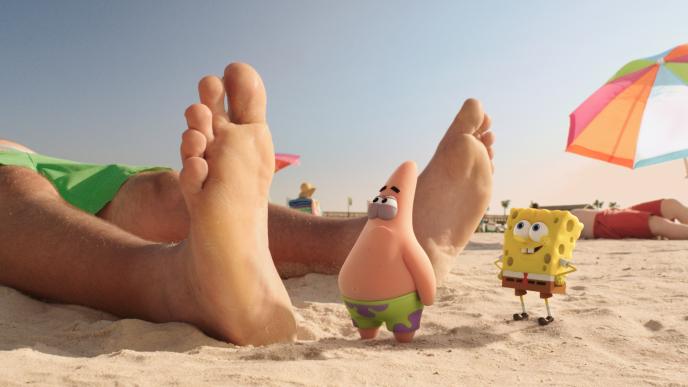 patrick the star fish and spongebob square pants standing next to a pair of legs and feet on a beach