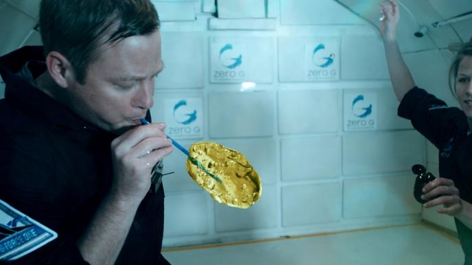 two astronoauts in zero gravity drinking squash that is floating in air