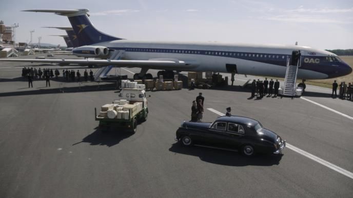 a plane on an airport runway. there is a car and a lorry surrounded with groups of people