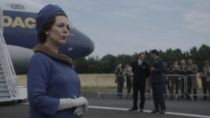 actress olivia colman as claire foy standing beside a private jet as a group of men stand in the background