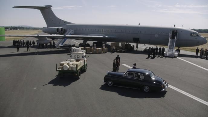 a plane on an airport runway. there is a car and a lorry surrounded with groups of people