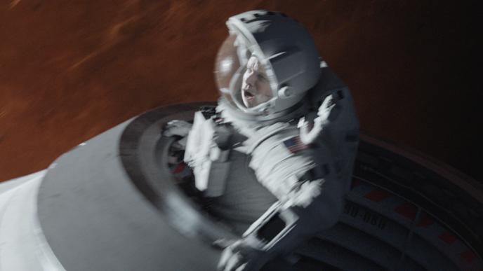 actor matt damon as character mark watney holding on and hanging out of a space shuttle. the background is red planet mars