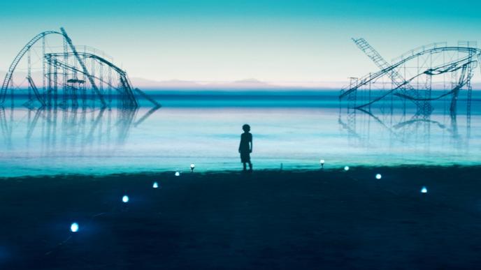 person standing in the centre of a beach looking out on to sea that has a broken and abandoned amusement ride