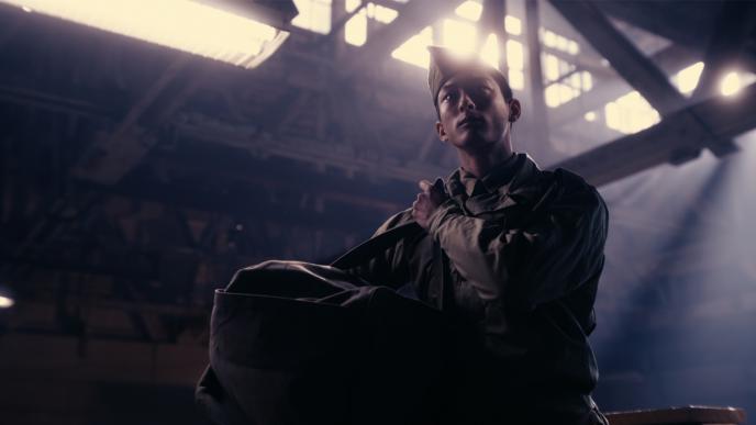 a japanese soldier holding a bag inside of a barn warehouse as light shine through the ceiling