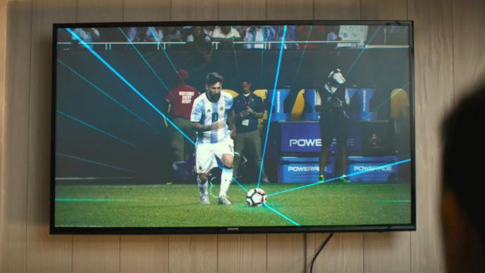 footballer messi on a television screen as he is about to shoot a ball on a football pitch 