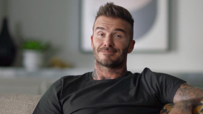 footballer david beckham sitting on a sofa looking directly at the camera with an aloof smile