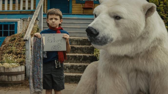 actor winslow fegley as timmy failure holding up a piece of paper with the words 'failure inc. official detective license' scribbled on it. there is a polar bear sitting next to him outside of a porch