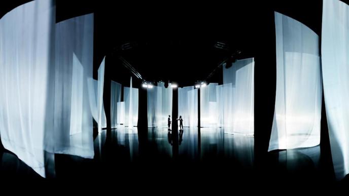two people standing in the centre of an exhibition that has full length sheer sheets hanging from the ceiling
