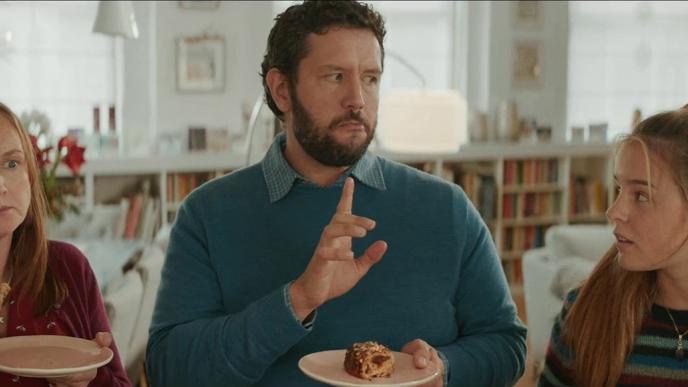 parents shushing their teenage daughter as they eat pork pies and she looks at them with a surprised expression