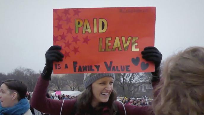 a person holding up a placard with the text 'paid leave is a family value' written on it