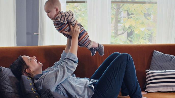a mother holding up a baby while laying on a sofa
