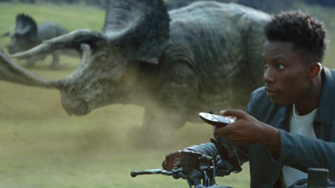 A man rides alongside dinosaurs, pointing a television remote