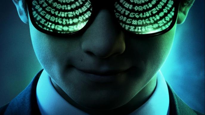 A boy in a dark suit wearing glasses reflecting green symbols