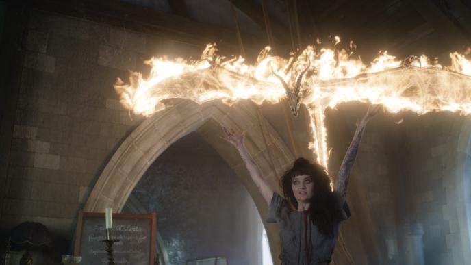 A student summons a fiery dragon, holding her arms above her head as it hovers above her