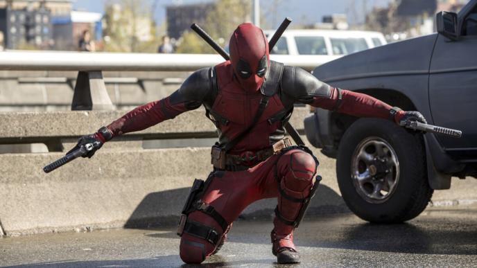 ryan reynolds as deadpool crouching down and holding out guns in both hands