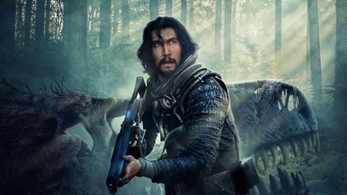 Adam Driver holds a large gun, standing in front of a dinosaur skull, in a forest