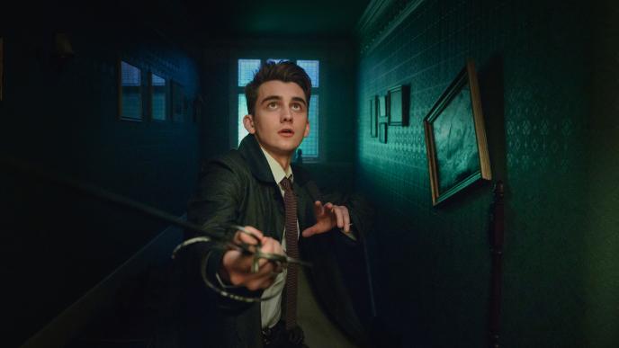 Lockwood stands alone in a dark hallway, looking upwards