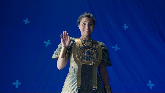 A actress, dressed as a goddess, waves awkwardly in front of a blue screen