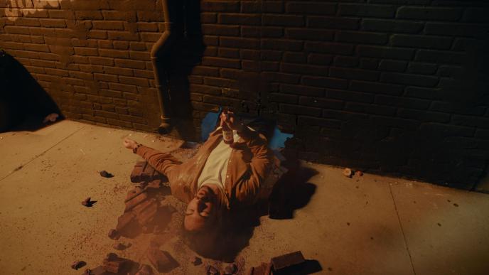 A man's head and torso sticks out from a brick wall as if he has fallen through it