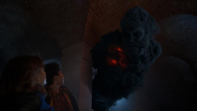 Lucy and George stand in a dark cellar, looking up at an enormous dark ghostly form