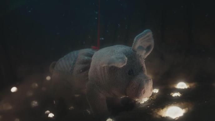 Cuddly toy Pig, in Netflix's Slumberland, sitting on sand, looking at small bright orbs