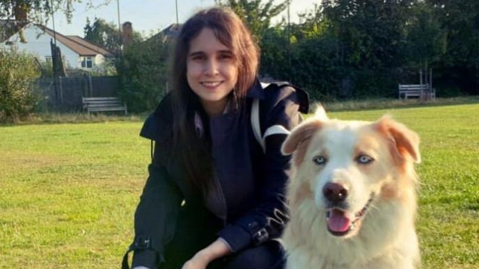 Gabriela Salmeron sits in a field, wearing a dark jacket, with a big white dog