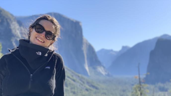 Charlotte Tyson sits outside, mountains in the background, wearing sunglasses