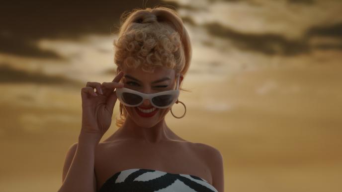 A still from Barbie showing Margot Robbie winking and lowering her sunglasses.