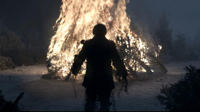 A raggedy silhouette of a man in front of a large bonfire