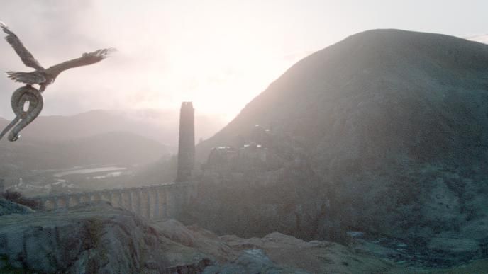 back view of an eagle soaring in the air over a bridge across mountainous terrain while holding a python snake
