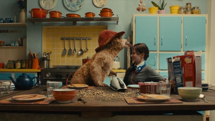 Paddington licks the forehead of a teenage girl, sat in a kitchen