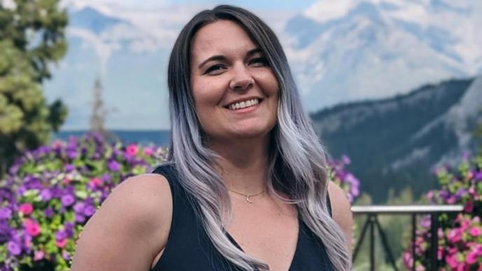 Sarah Johnson sits outside, with a blue sky and colourful flowers in the background