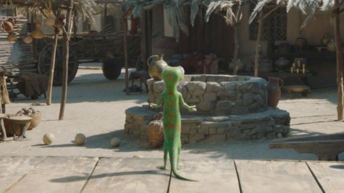 The GEICO gecko stood in front of a well in a market area.
