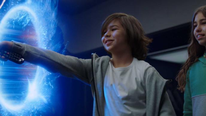 A young boy and a girl using a Sky TV remote, there is a glowing blue ring-shaped portal.