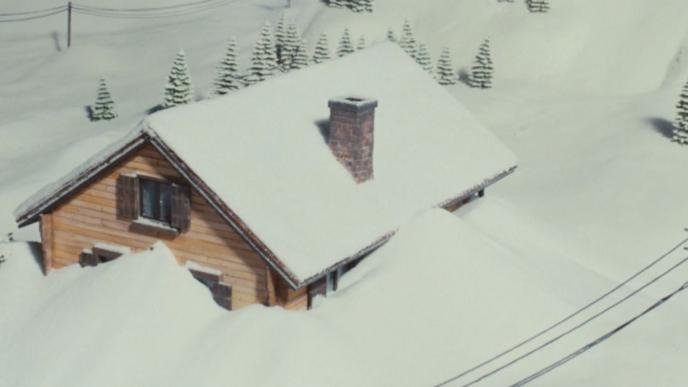 A cabin in the mountains is covered in snow from an avalanche.