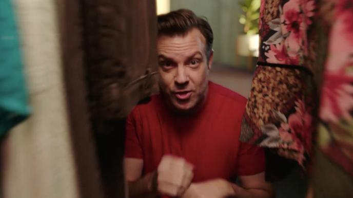 A person inside of a closet in between clothes. The outer corners of the image have been blurred